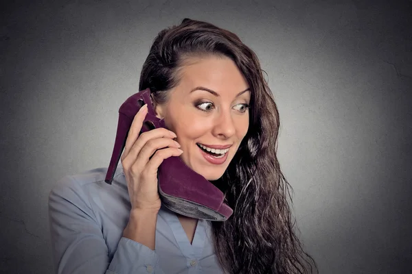 Young surprised woman holding high heeled shoe in hand as phone — Stockfoto