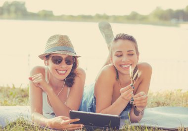 young women friends laughing watching social media blogs on pad computer