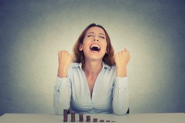 successful business woman sitting at table with growing stack of coins