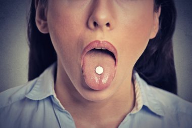 Closeup cropped image of young woman with white pill on her tongue