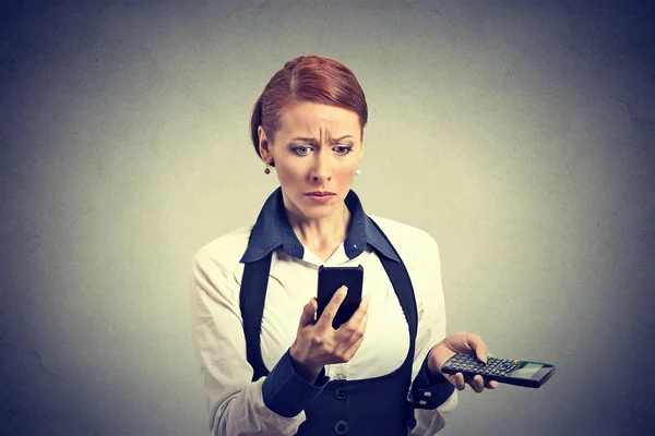 Upset business woman looking at smart phone holding calculator — Stockfoto