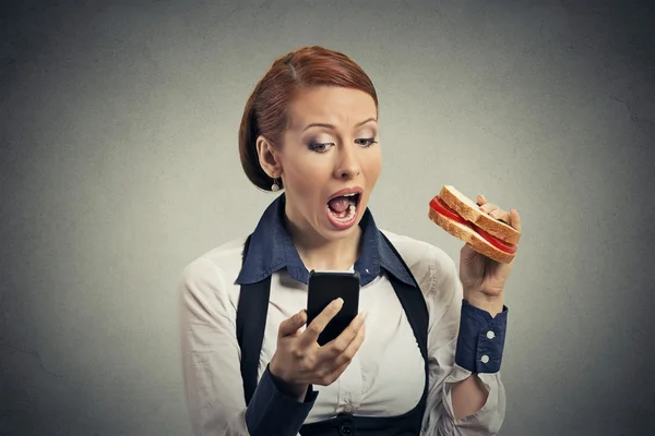 Geschäftsfrau liest Nachrichten auf Smartphone und isst Sandwich — Stockfoto