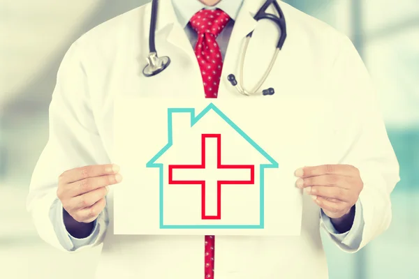 Doctor hands holding white paper house with red cross sign — Stock Fotó