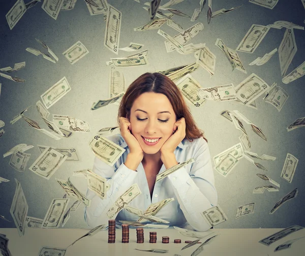 Woman sitting at table with growing stack of coins under a money rain — Stock Photo, Image