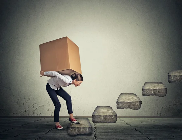 Difficult task concept. Young woman carrying heavy box upstairs — Stockfoto