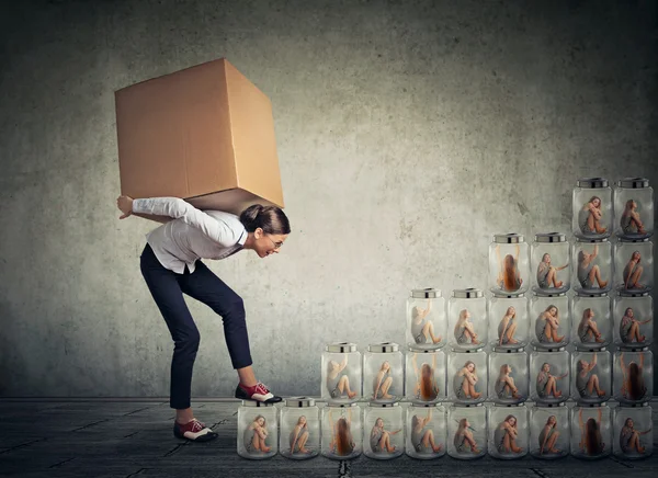 Woman with big box on her back climbing up a stair made of jars with women inside — Stock fotografie