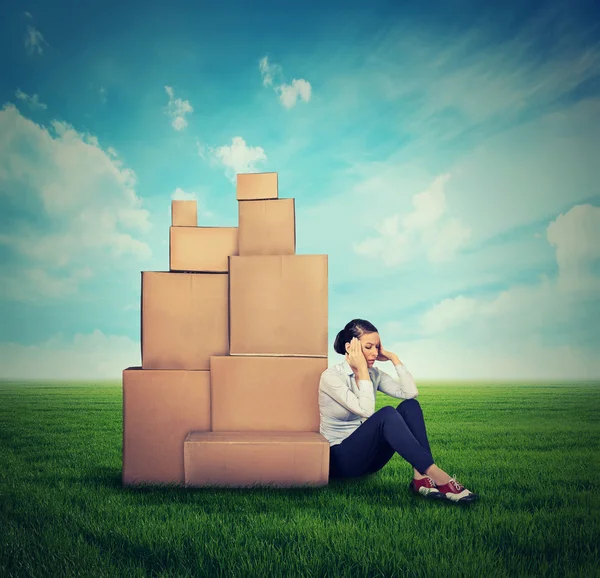 Young stressed woman sitting on the ground green grass with many boxes — Φωτογραφία Αρχείου