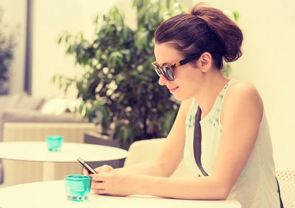 Chica feliz mensajes de texto en el teléfono inteligente en una terraza restaurante del hotel —  Fotos de Stock