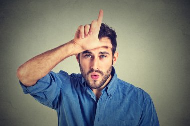 young man showing loser sign on forehead, looking at you with disgust