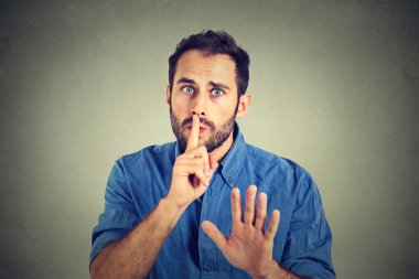 man giving Shhhh quiet, silence, secret gesture isolated on gray wall background