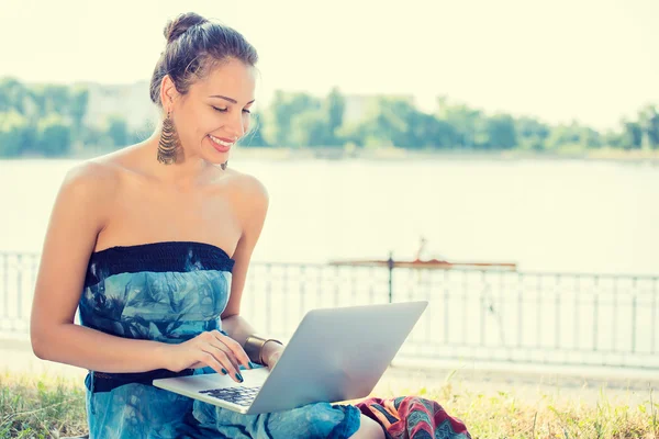Mujer joven divertida trabajando con su portátil portátil sentado en un césped —  Fotos de Stock