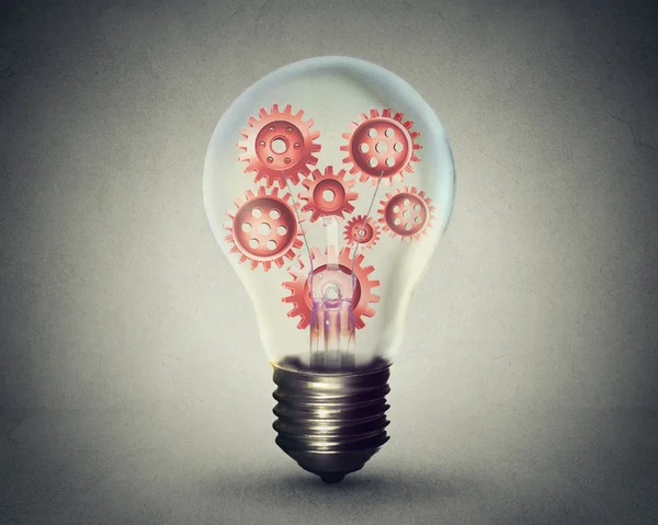 Light bulb with gears and cogs working together on gray wall background — ストック写真