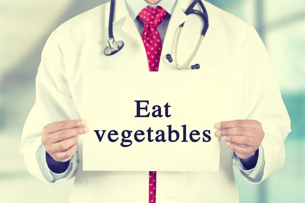 Doctor hands holding white card sign with eat vegetables text message — Zdjęcie stockowe