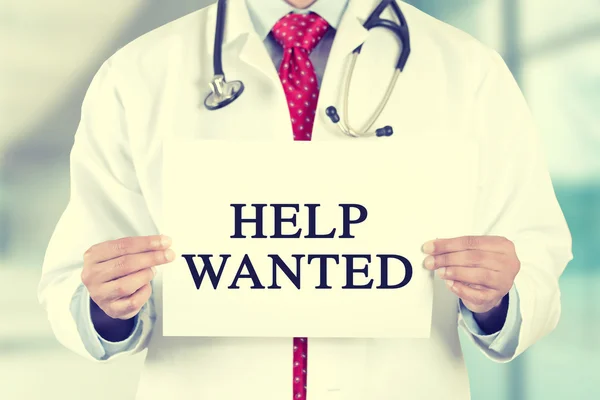 Doctor hands holding white card sign with help wanted text message — 图库照片