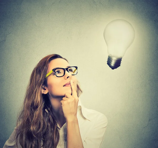Girl thinks looking up at bright light bulb — Stock Photo, Image