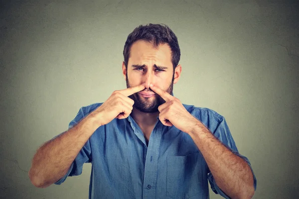 Disgusted man pinches nose with fingers hands looks with disgust something stinks — Stock Photo, Image