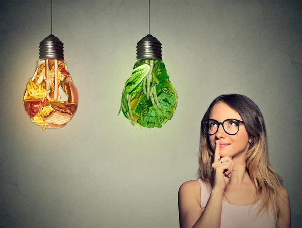 Vrouw denken kijken op junkfood en groene groenten gevormd als gloeilamp — Stockfoto