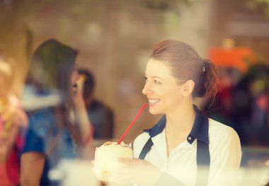 woman drinking coconut juice, looking outside on street through glass window