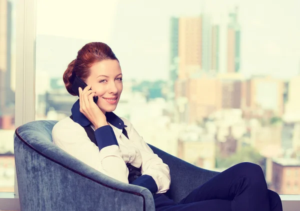 Business woman talking on mobile phone siting in armchair by the office window — Stock Photo, Image