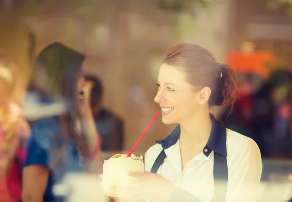 Woman drinking coconut juice, looking outside on street through glass window — Stock Photo, Image