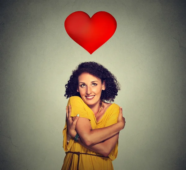 Portrait smiling woman holding hugging herself with red heart above head — Stock Photo, Image