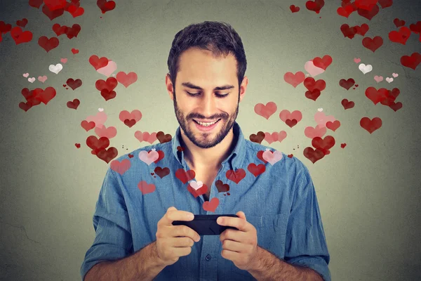 Hombre enviando mensaje de amor sms en el teléfono móvil con corazones que vuelan lejos —  Fotos de Stock