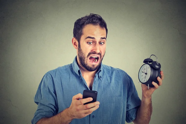 Surprised business man with alarm clock looking at smart phone — Stock Photo, Image