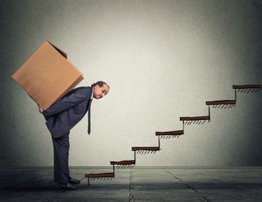 Middle aged business man carrying large heavy box on his back upstairs