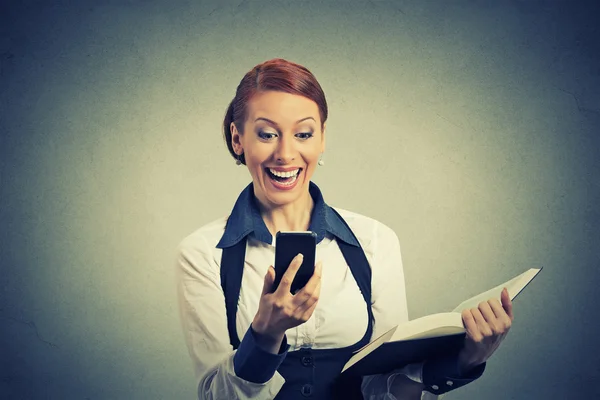 Happy young woman holding book looking at phone seeing good news — Stock Photo, Image