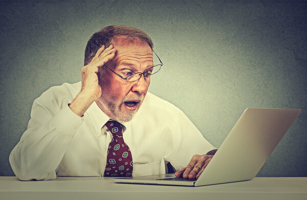 беспокойный старший мужчина смотрит на экран ноутбука и видит плохие новости с отвратительными эмоциями на лице
