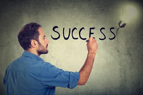 Perfil lateral jovem homem escrevendo sucesso em uma parede cinza — Fotografia de Stock