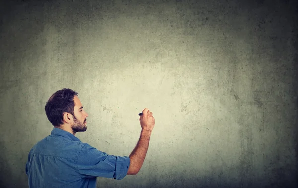 Hombre de negocios joven empresario escribiendo en una pared gris con pluma —  Fotos de Stock