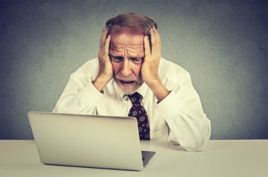 senior stressed man working on laptop sitting at table isolated on gray wall background  clipart
