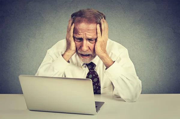 Senior benadrukt man aan het werk op laptop zitten aan tafel geïsoleerd op grijze muur achtergrond — Stockfoto