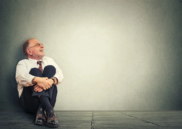 Thinking senior man sitting on floor. Mature corporate executive  smiling looking up dreaming — Stock Photo, Image