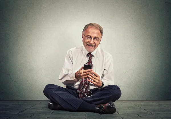 Senior executive man sitting on a floor using smart phone texting listening music — Stock Photo, Image