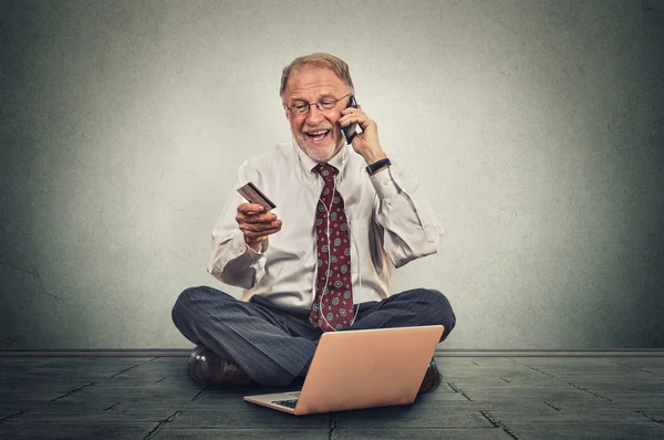Улыбающийся пожилой человек делает заказ по мобильному телефону, сидя на полу своего офиса — стоковое фото