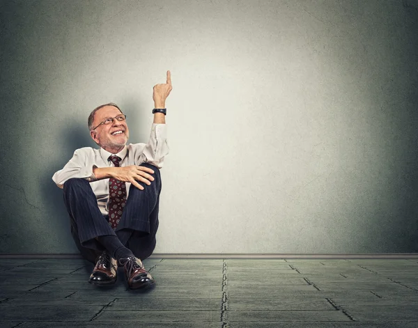 Senior happy man sitting on floor with legs crossed and pointing up — ストック写真