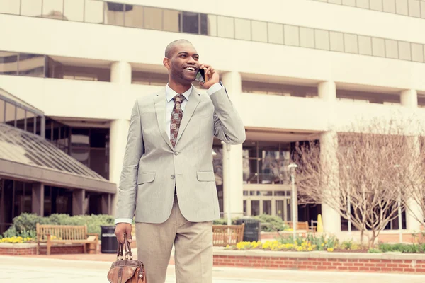 Smiling business man talking on mobile phone holding briefcase walking down the street — Zdjęcie stockowe