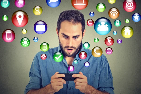 Shocked man using texting on smartphone application icons flying out of cellphone — Stockfoto