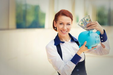 happy successful young business woman depositing money dollars in piggy bank