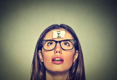 Thinking young woman with sand clock sign sticker on her forehead
