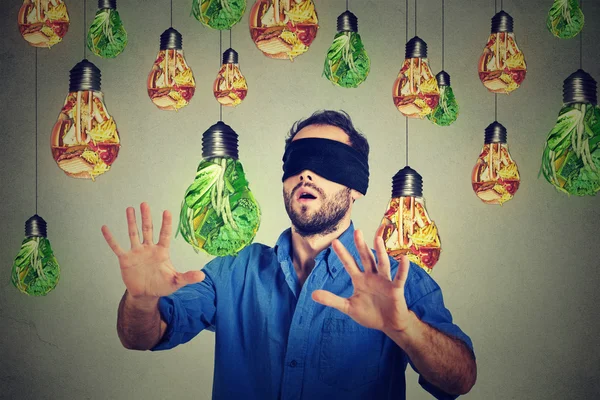 Blindfolded man walking through light bulbs shaped as junk food and green vegetables — Stockfoto