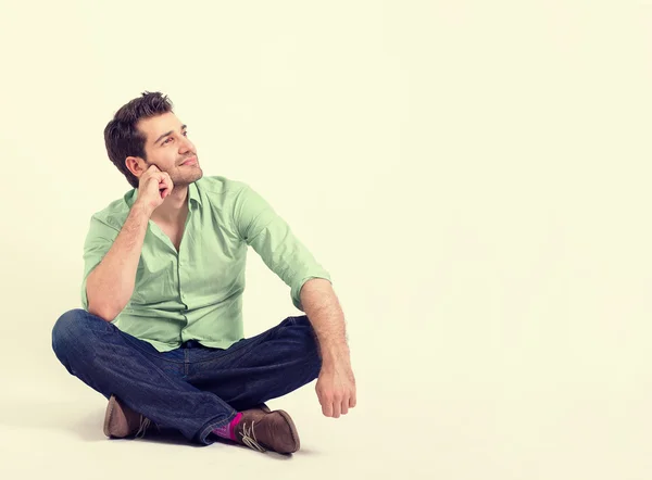 Щасливий молодий чоловік в зеленій сорочці і блакитних джинсах сидить на підлозі — стокове фото
