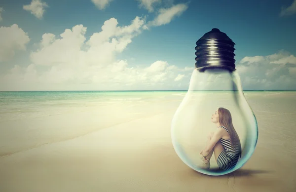 Woman sitting inside a light bulb on a beach looking at the ocean view — Stock Photo, Image