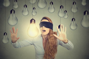 Blindfolded young woman walking through lightbulbs searching for bright idea 