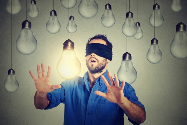 Blindfolded man walking through lightbulbs searching for bright idea — Stock Photo, Image