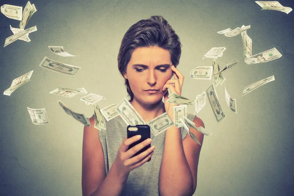 Thoughtful young woman using smartphone with dollar bills banknotes flying away — Stok fotoğraf