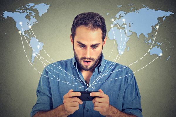 Шокированный молодой бизнесмен держит в руках смартфон
