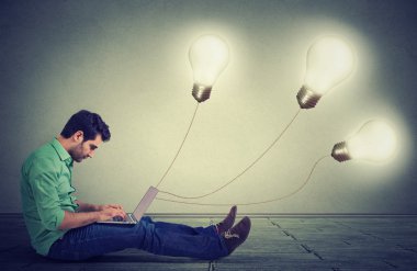 Side profile man sitting on floor using a laptop with many light bulbs plugged in it